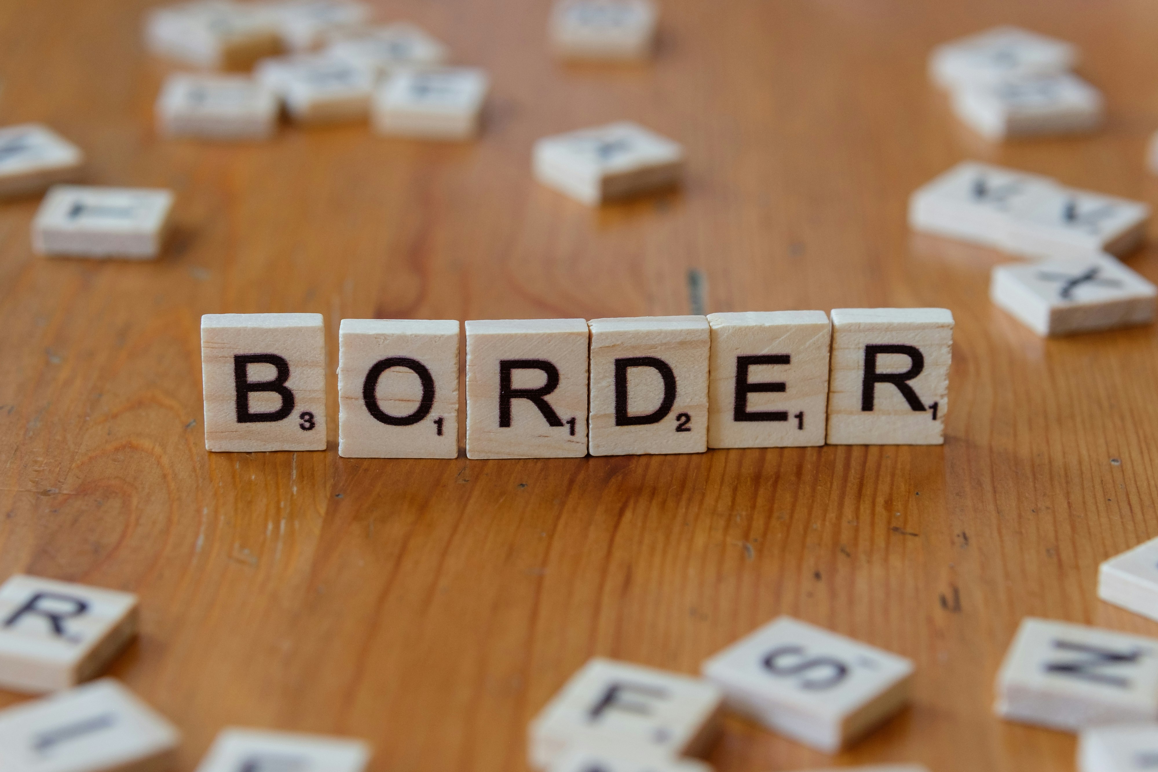 Scrabbled letters spelling the word border on a wooden table